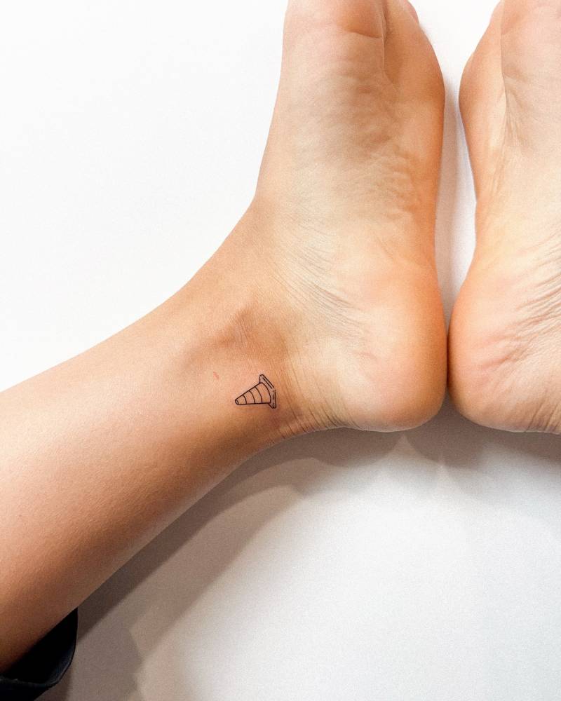 Little traffic cone tattoo in fine line style located on the ankle.