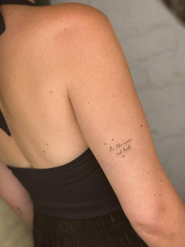 Handwritten font "to the moon and back" lettering tattoo located on the tricep.