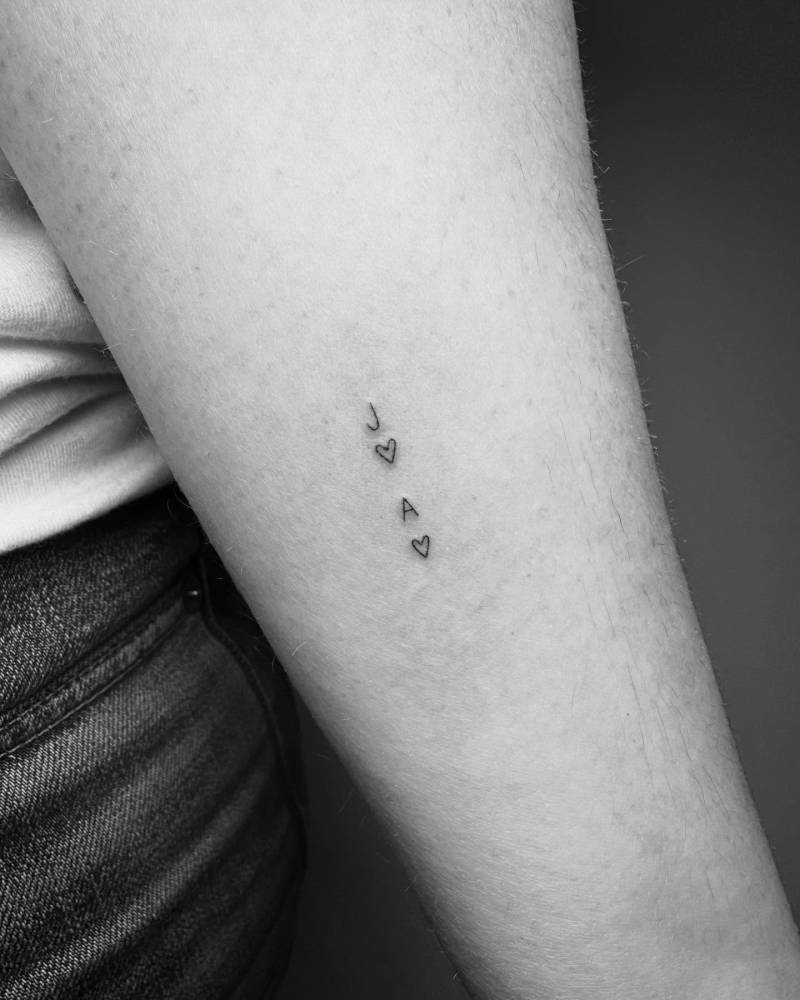 Letters "A" and "J" with hearts tattooed on the inner forearm.