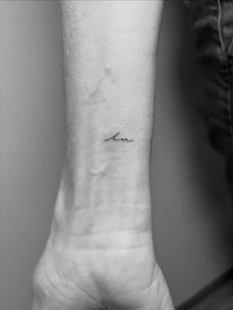 Minimalistic style initials in handwritten font tattooed on the wrist.