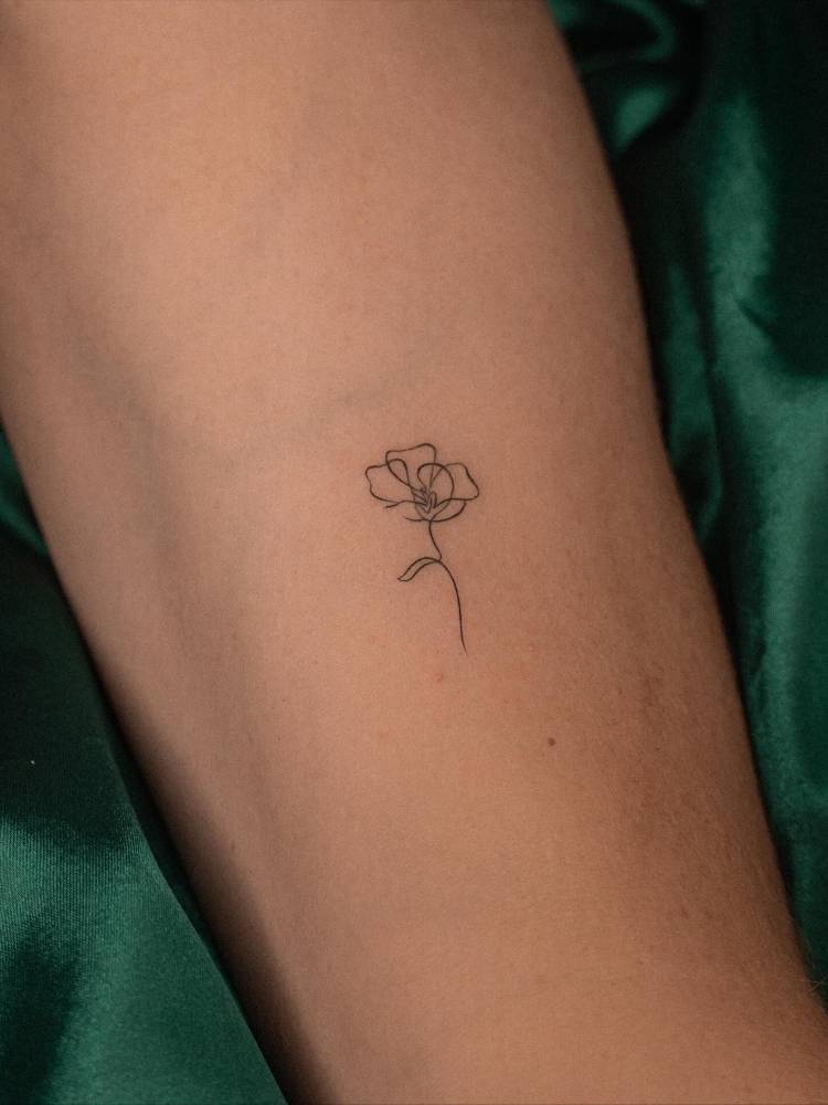 One line flower tattoo located on the inner forearm.