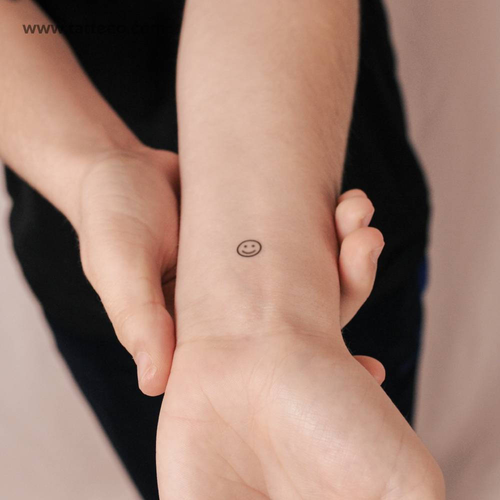 Minimalist smiley semi-permanent tattoo located on the wrist.