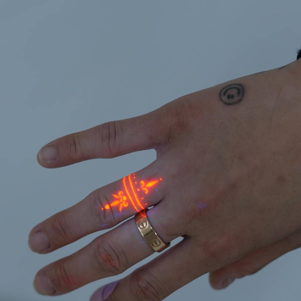 UV ink ornamental red ring tattoo located on the finger.
