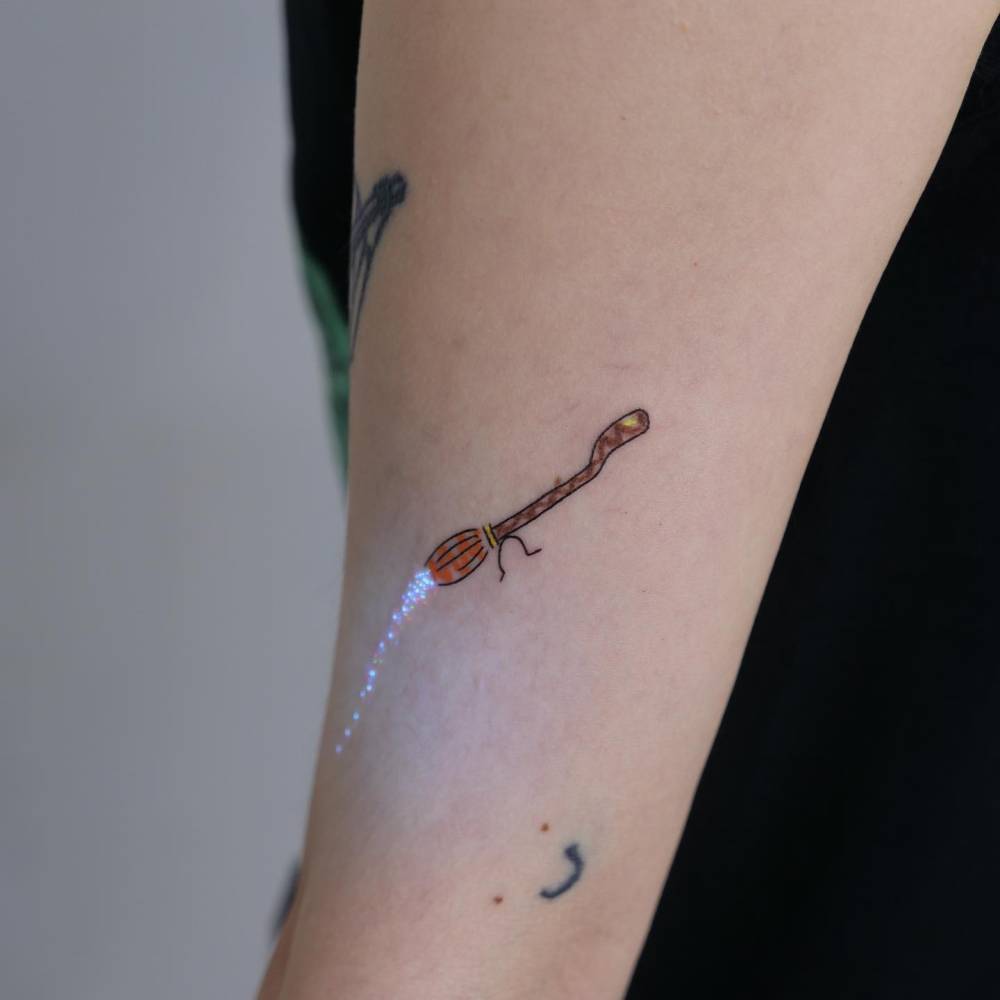 Flying broom tattoo located on the inner forearm.