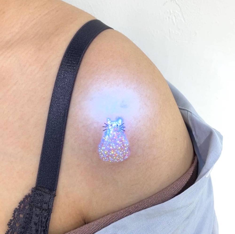 Glittery cat tattoo in uv ink located on the shoulder.