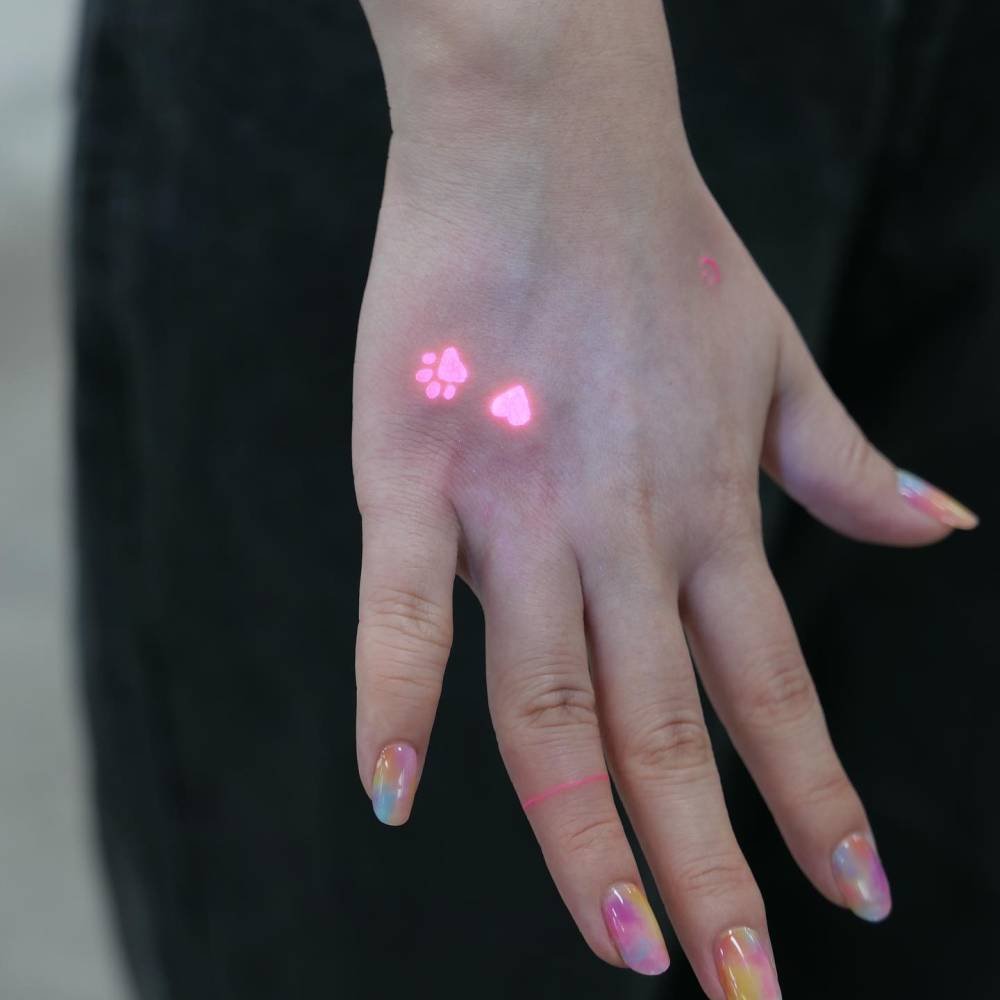 UV ink dog paw and heart tattooed on the hand, minimalistic style.