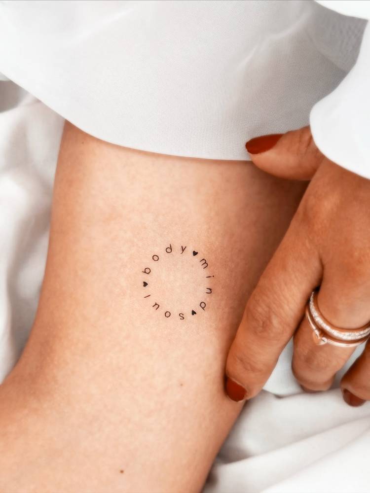 “Body, mind, soul” lettering circle tattooed on the inner arm.