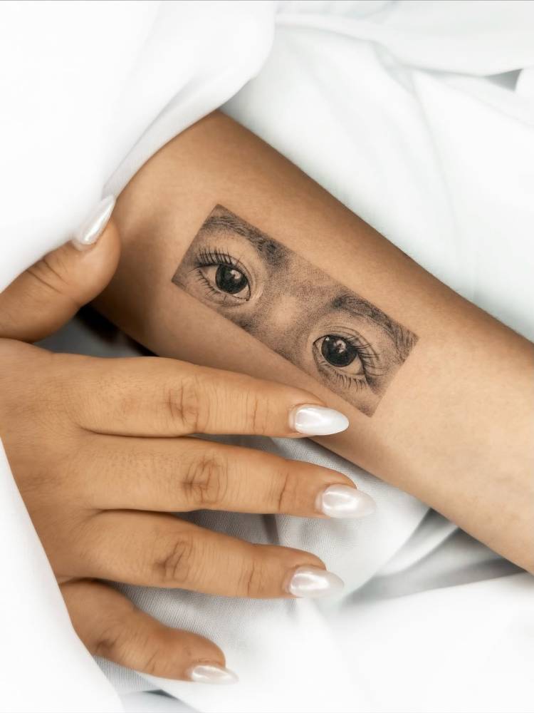 Micro-realistic style eyes tattoo located on the inner forearm.