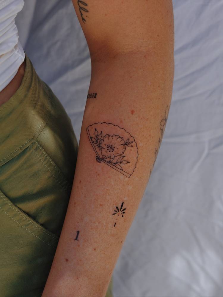 Floral hand fan tattoo located on the forearm.