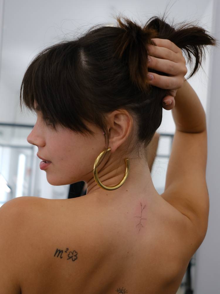 Sprout tattoo in fine line style located on Martina Cariddi's upper back.