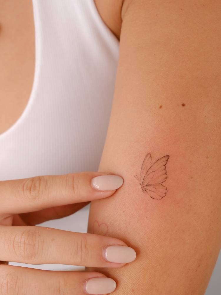 Little butterfly tattoo in fine line style placed on the upper arm.