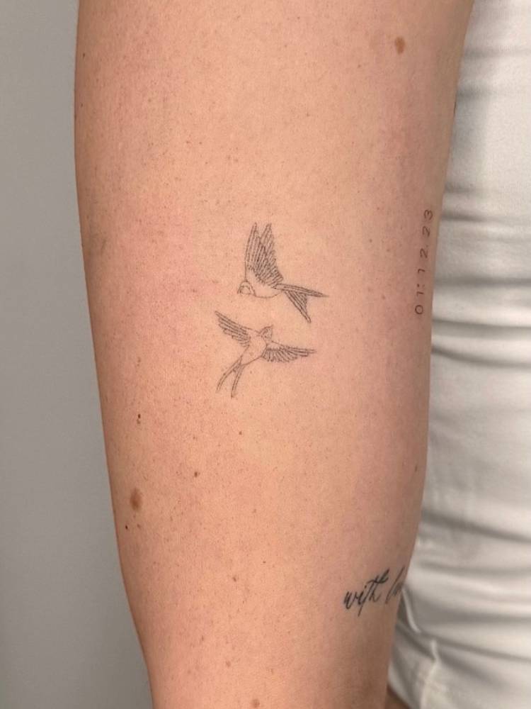 Single needle flying swallows tattoo located on the upper arm.