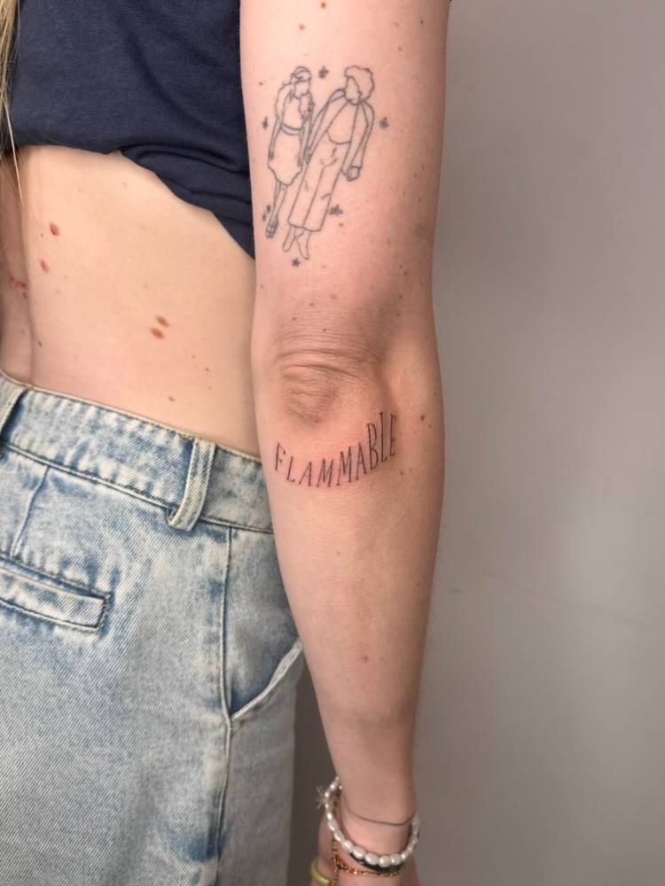 Serif font word "flammable" tattooed on the elbow.