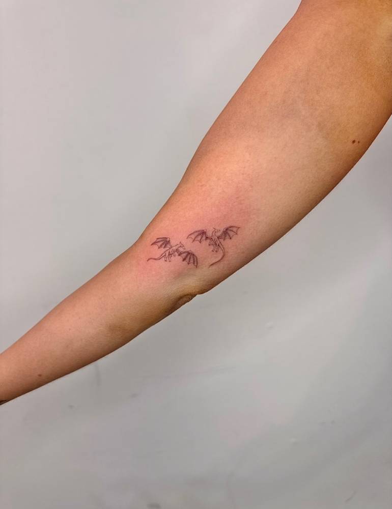 Little dragons tattoo in fine line style located on the inner arm.