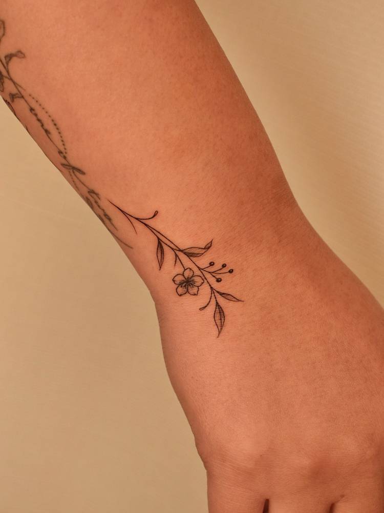 Tiny flower tattoo located on the wrist, illustrative style.