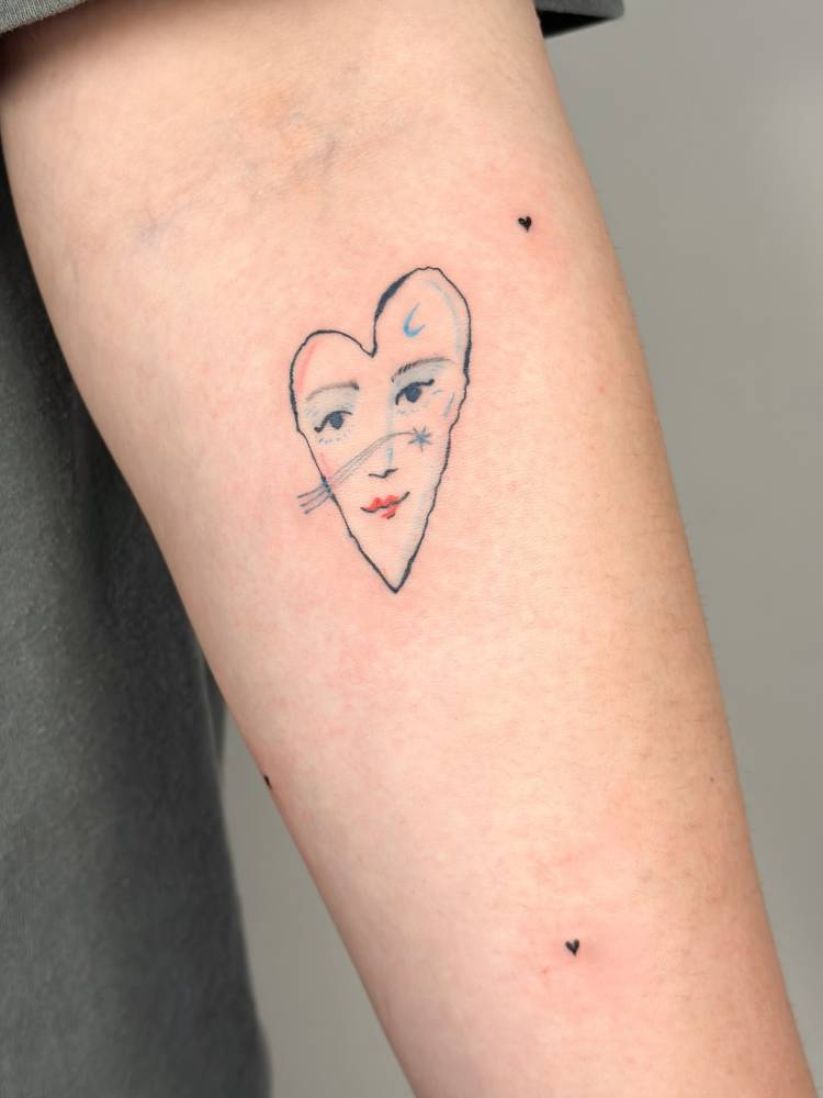 Heart face tattoo located on the inner forearm.