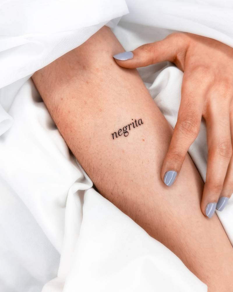 "Negrita" lettering tattoo in serif font located on the inner forearm.
