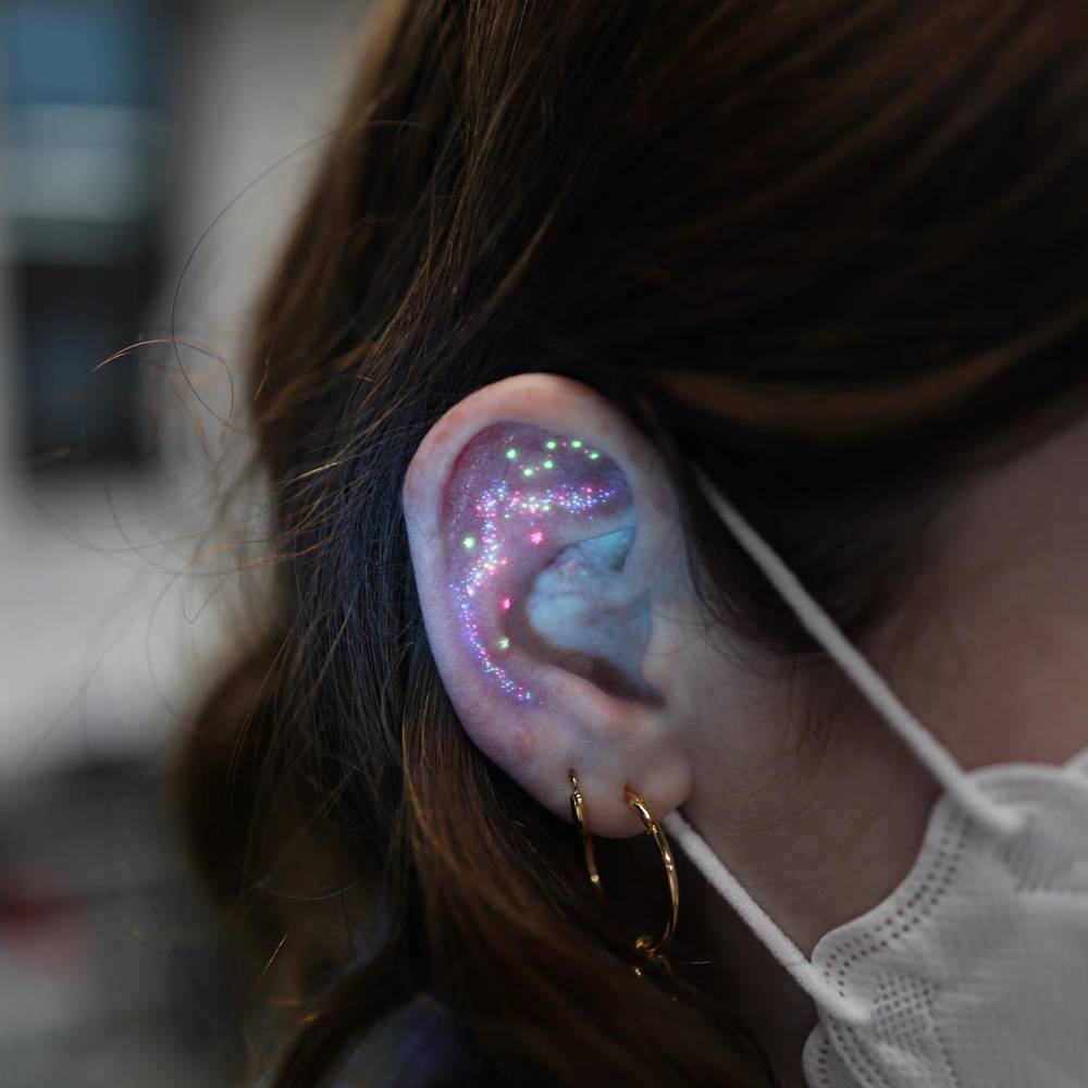 Glitter effect UV ink tattoo located on the ear.