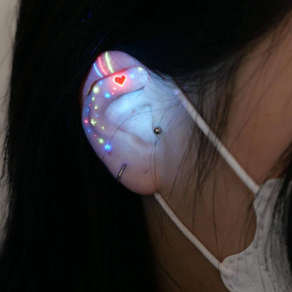 Heart and stars tattoo in UV ink placed on the ear.