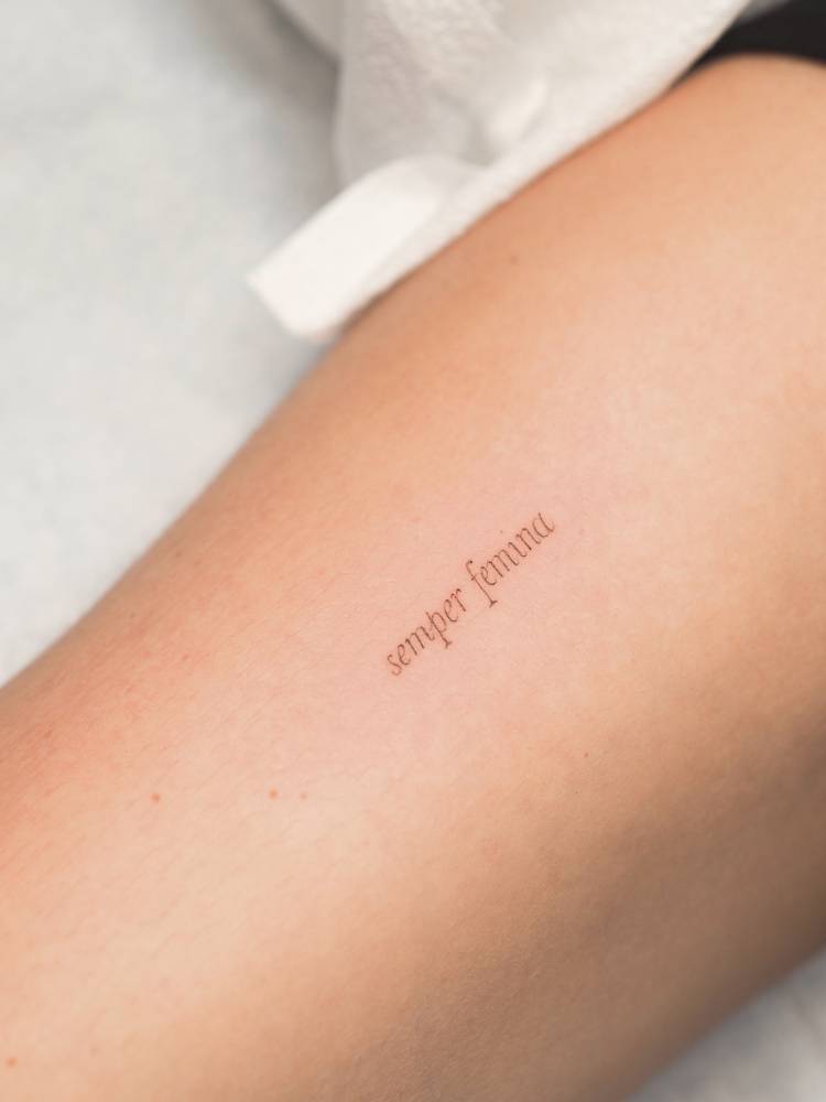 "Semper femina" lettering tattoo located on the inner arm.