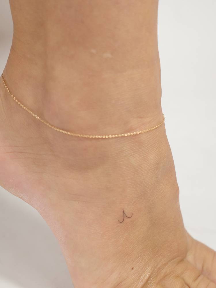 Tiny minimalistic Aries zodiac symbol tattooed on the foot.
