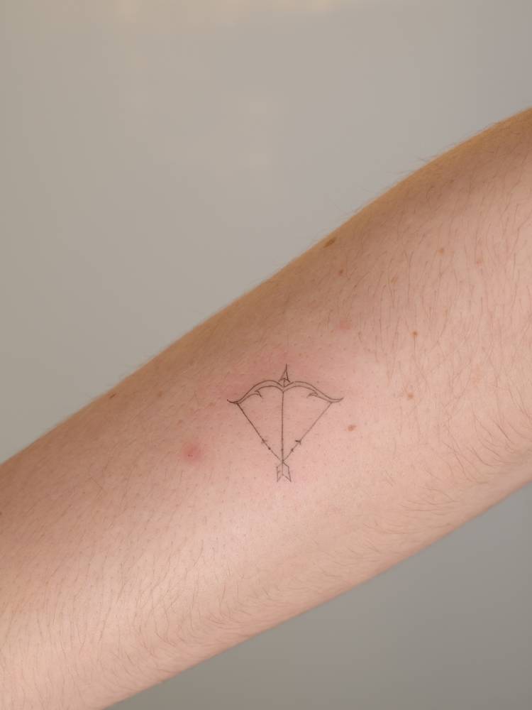 Bow and arrow tattoo in fine line style located on the forearm.