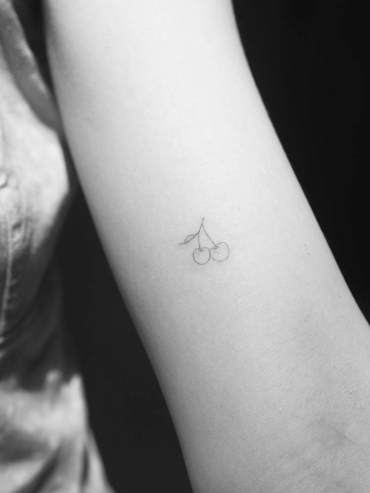 Tiny cherries tattooed on the bicep, fine line style.
