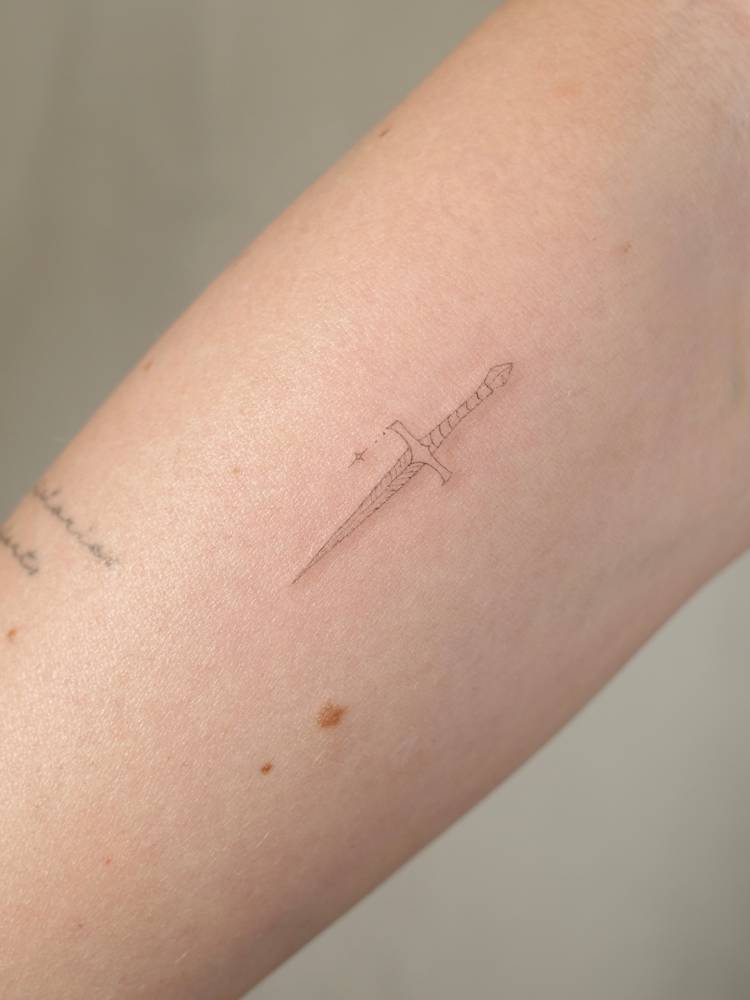 Dagger tattoo in fine line style located on the inner forearm.