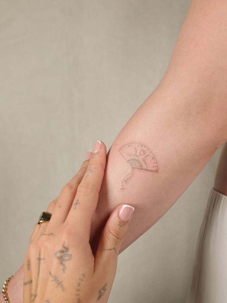 Hand fan tattoo located on the forearm, done in fine line style.