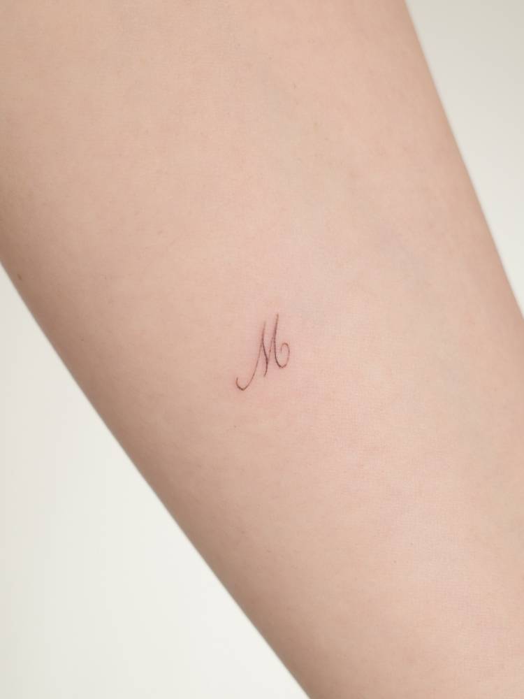 Little initial "M" in script font tattooed on the inner forearm.