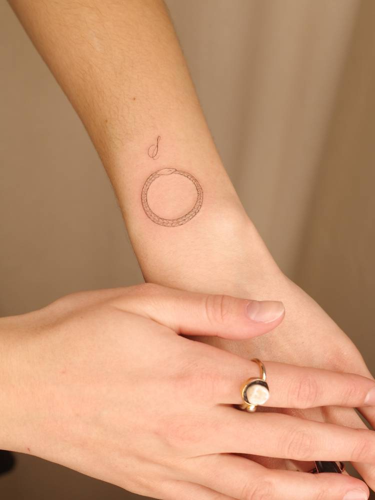 Snake ouroboros tattoo placed on the wrist, fine line style.