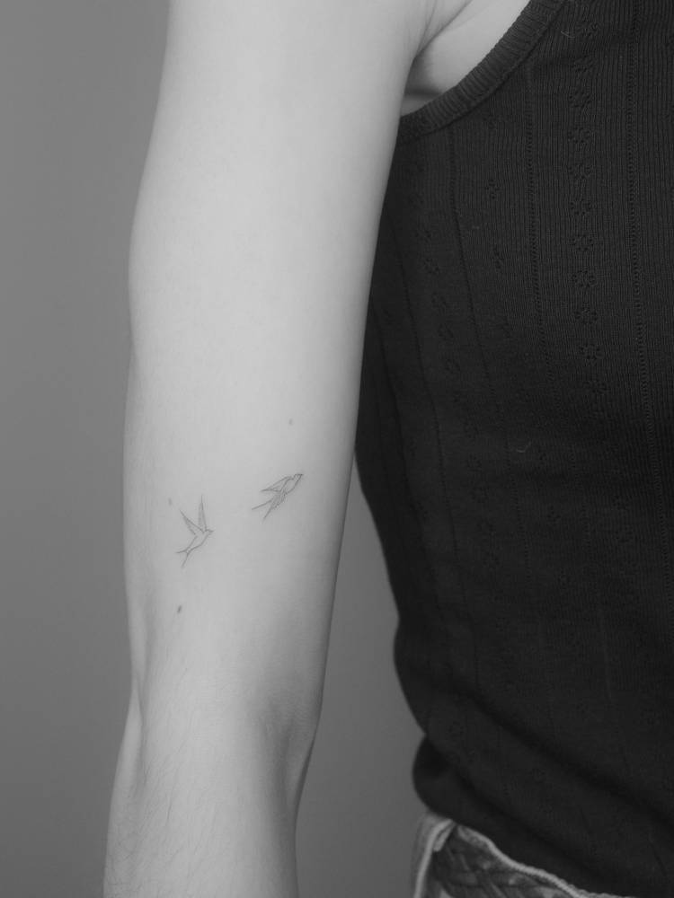 Tiny flying swallows tattoo located on the upper arm.