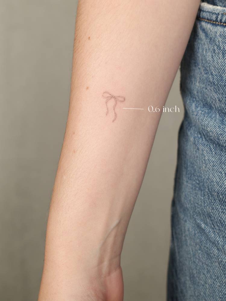 Bow tattoo located on the inner forearm, done in fine line style.