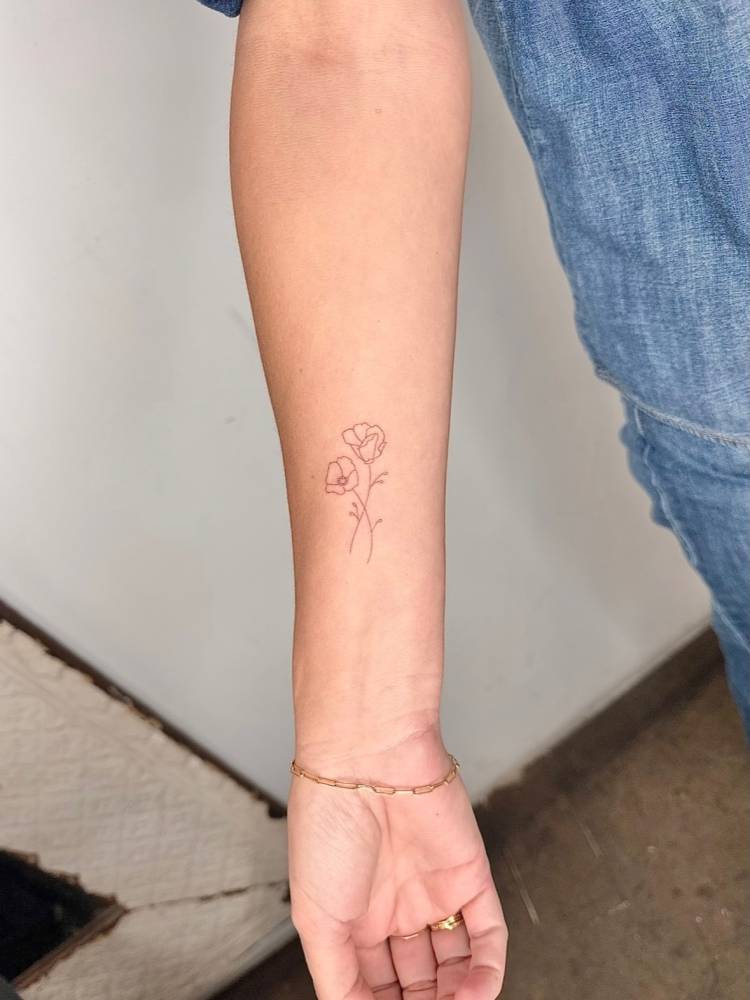 Poppy flowers tattooed on the inner forearm, done in fine line style.