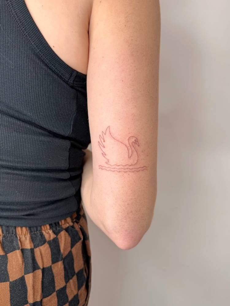 Fine line style swan tattoo located on the tricep.
