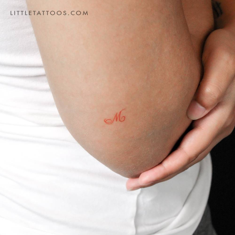 Little red letter "M" script temporary tattoo located on the tricep.