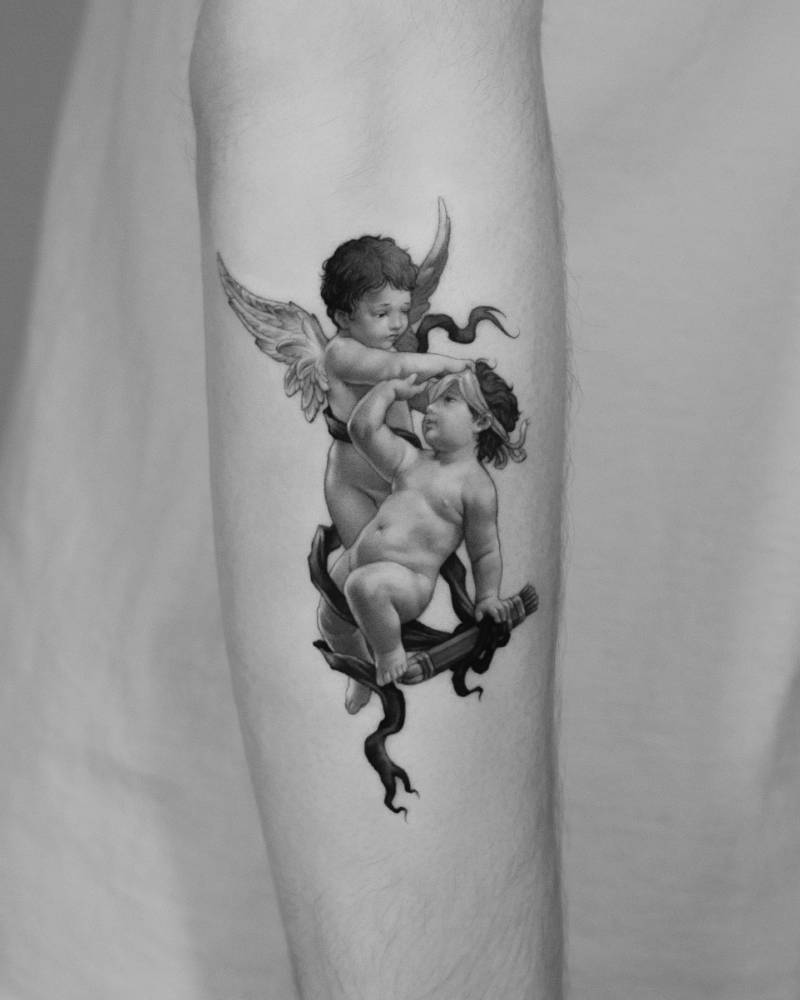 Classical style cherubs tattoo located on the forearm.