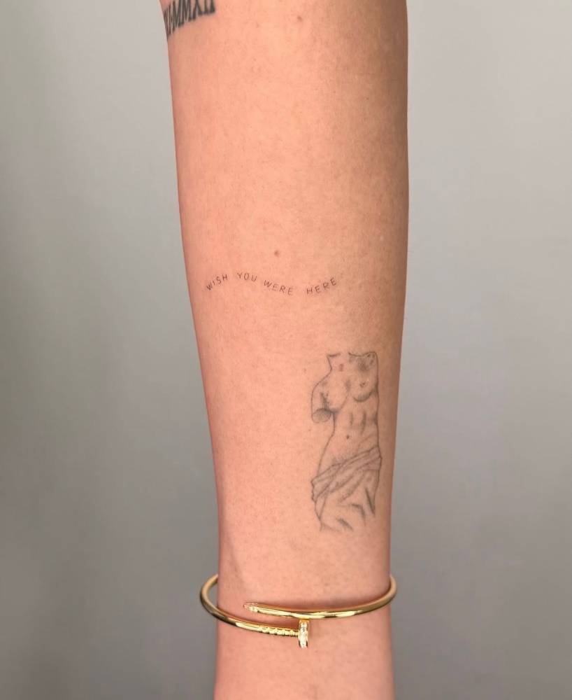 "Wish you were here" lettering tattoo located on the forearm.