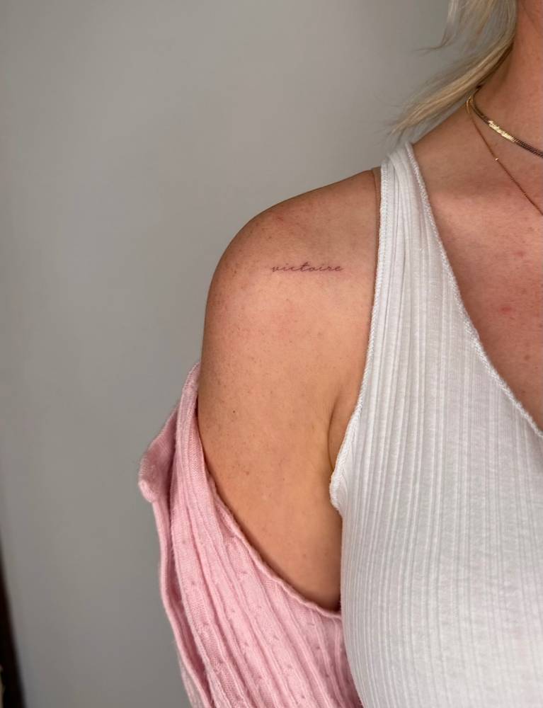 "Victoire" lettering tattoo placed on the shoulder.