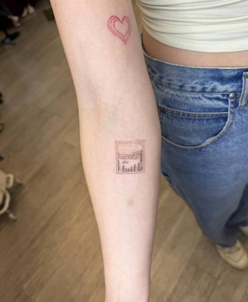 Mountain landscape stamp tattoo located on the inner forearm.