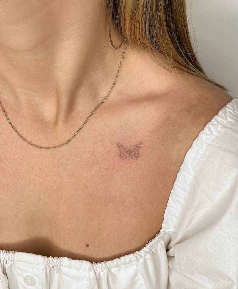 Little butterfly tattoo in fine line style placed on the collarbone.