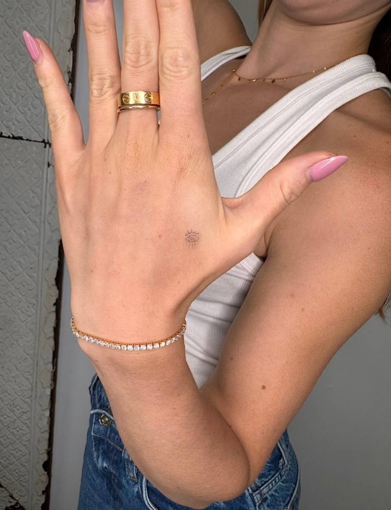 Micro evil eye tattooed on the hand, fine line style.
