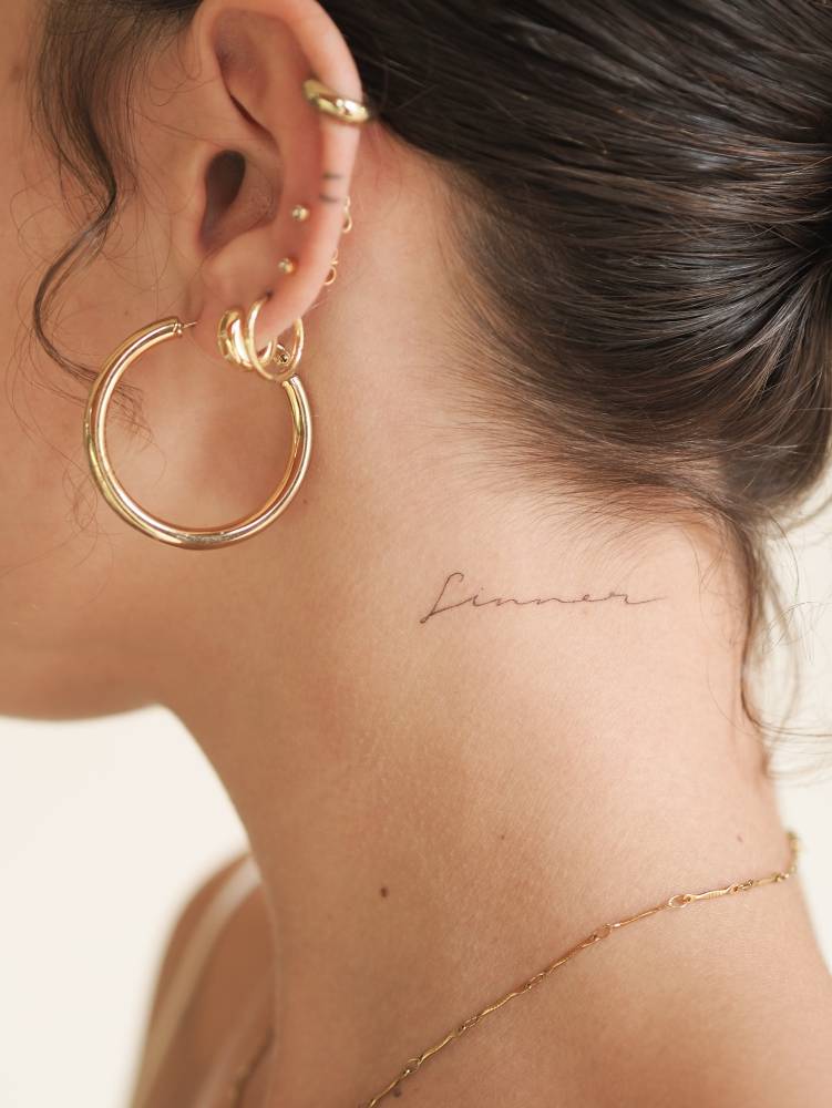 Handwritten font word "sinner" tattoo done on the neck.