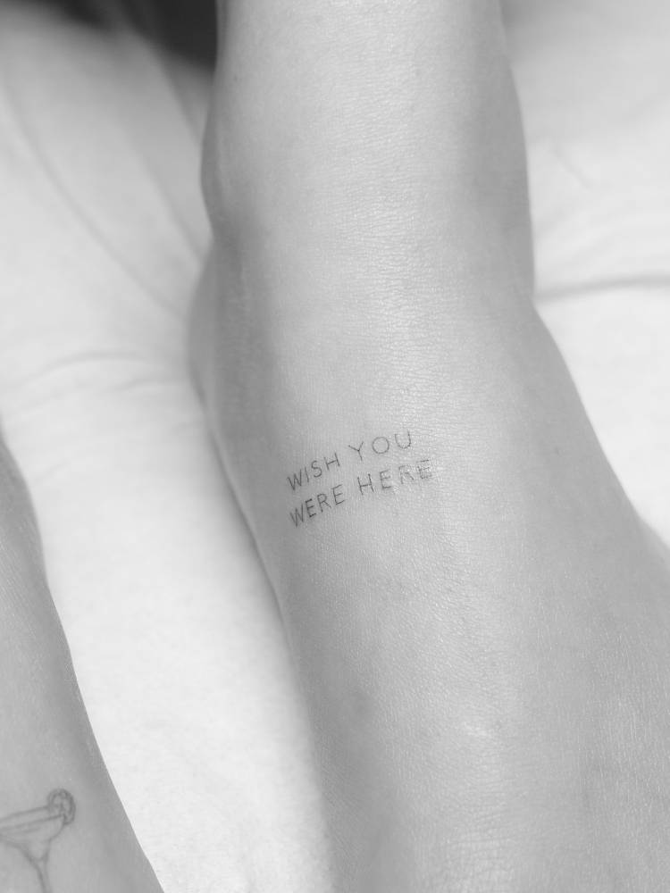 "Wish you were here" lettering tattoo located on the foot.