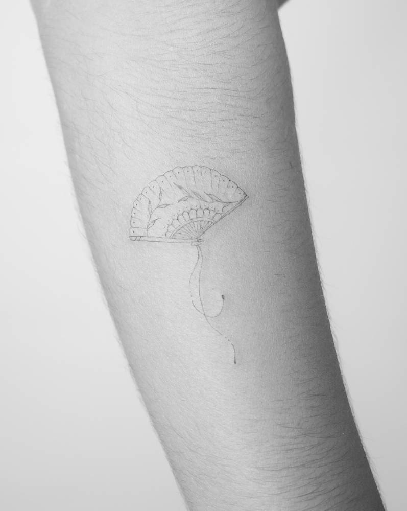 Cute hand fan tattoo in fine line style located on the forearm.