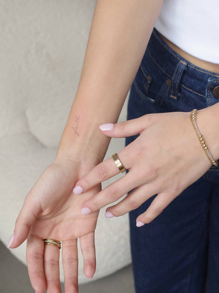 Handwritten font word faith tattooed on the wrist.