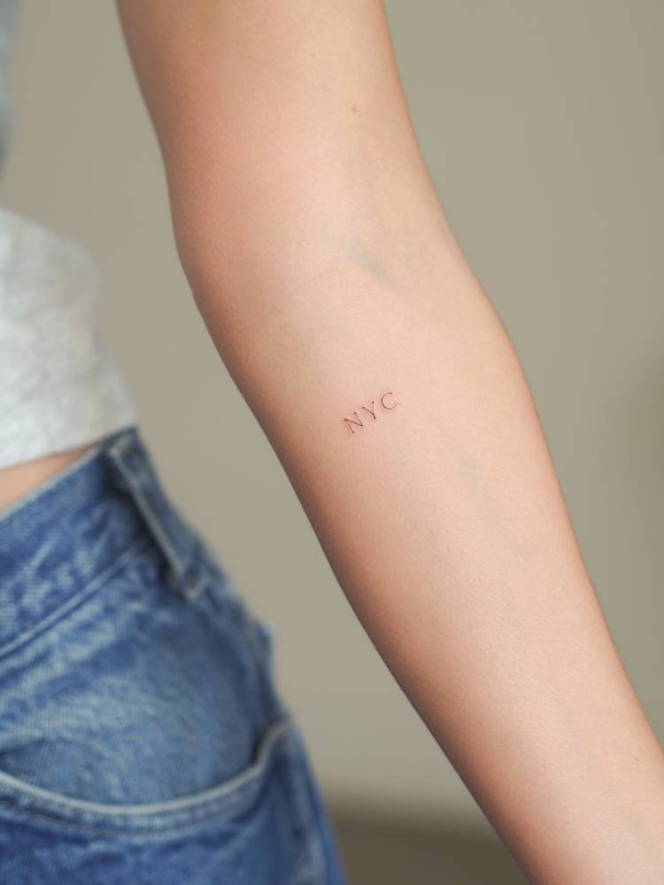 Serif font "NYC" lettering tattoo located on the inner forearm.