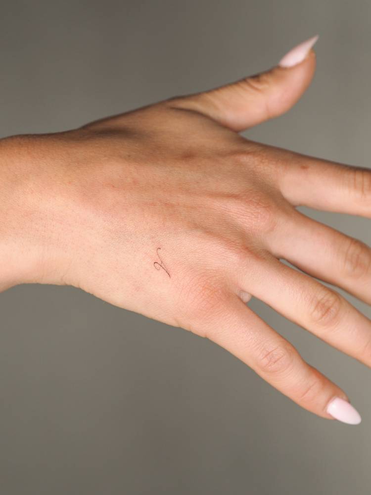 Script font tiny letter "A" tattoo located on the hand.