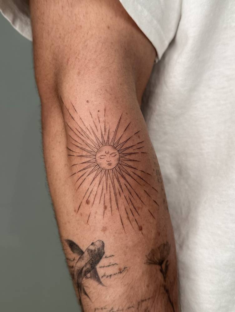 Inti sun tattoo located on the forearm, illustrative style.
