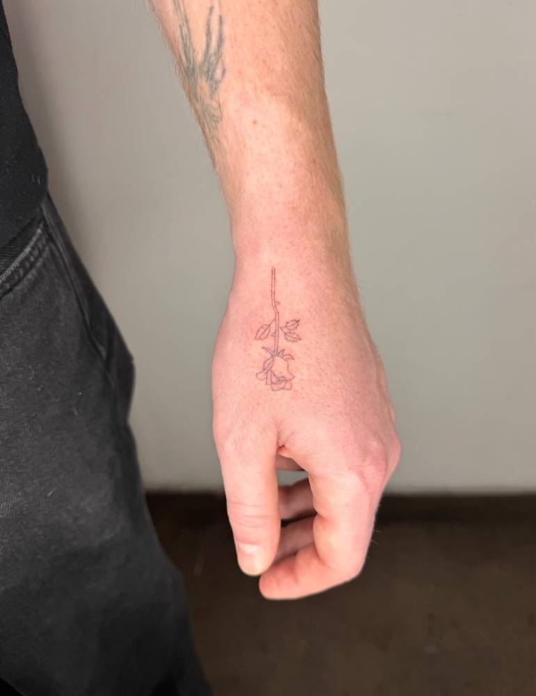 Single needle tattoo of a rose located on the hand.